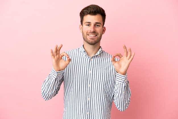Jonge blanke knappe man geïsoleerd op roze achtergrond met ok teken met twee handen