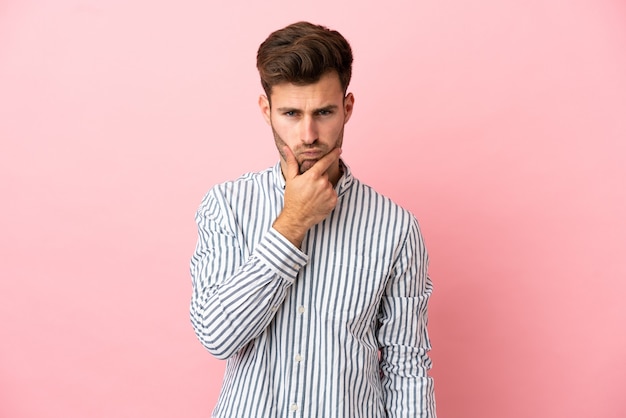 Jonge blanke knappe man geïsoleerd op roze achtergrond met twijfels