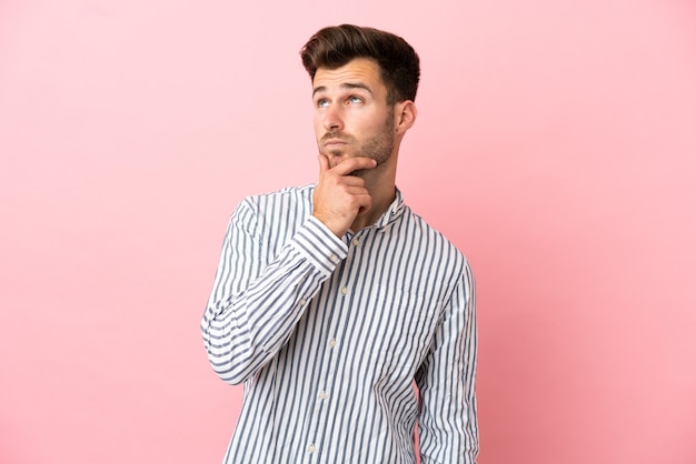 Jonge blanke knappe man geïsoleerd op roze achtergrond met twijfels