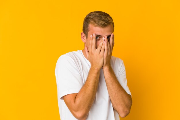 Jonge blanke knappe man knippert met zijn vingers naar de camera, beschaamd bedekkend gezicht.