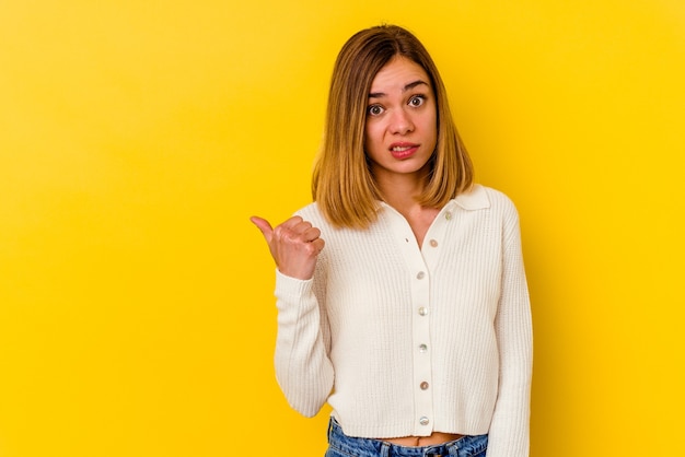 Jonge blanke magere vrouw geïsoleerd op geel geschokt wijzend met wijsvingers naar een kopie ruimte.