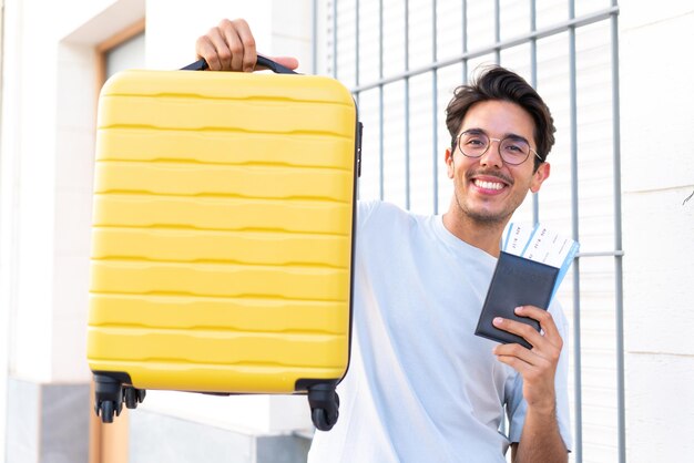 Jonge blanke man buitenshuis in vakantie met koffer en paspoort