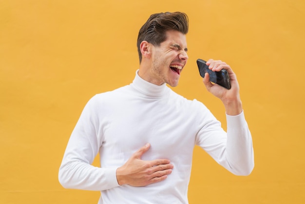 Jonge blanke man buitenshuis met behulp van mobiele telefoon en zingen