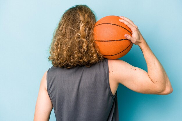 Jonge blanke man die basketbal speelt geïsoleerd op blauwe achtergrond