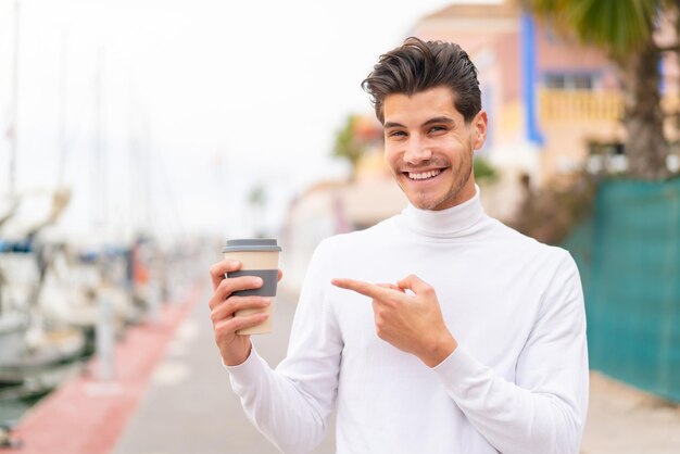 Jonge blanke man die buitenshuis een afhaalkoffie vasthoudt met een gelukkige uitdrukking