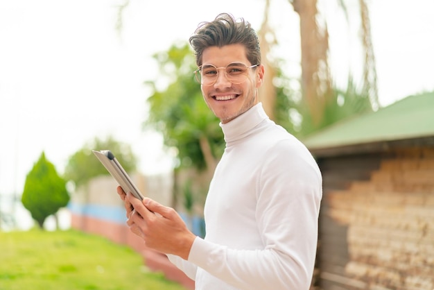 Jonge blanke man die buitenshuis een tablet vasthoudt met een gelukkige uitdrukking