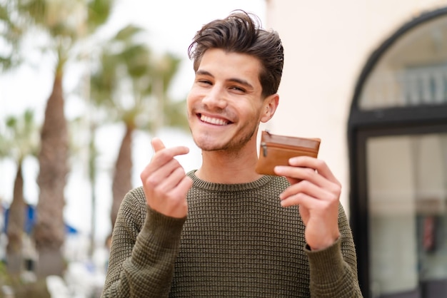 Jonge blanke man die buitenshuis portemonnee vasthoudt met geldgebaar