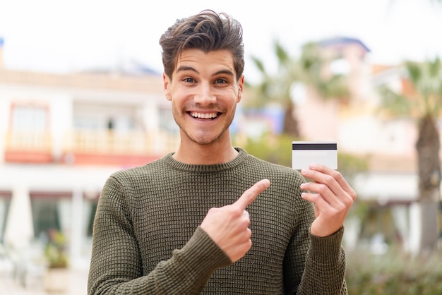 Jonge blanke man die een creditcard naar buiten houdt en erop wijst