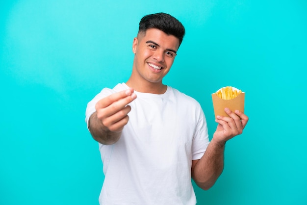 Jonge blanke man die frietjes vangt die op een blauwe achtergrond worden geïsoleerd en geld maakt gebaar