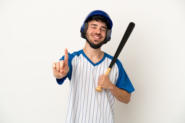 Jonge blanke man die honkbal speelt geïsoleerd op een witte achtergrond die een vinger laat zien en optilt