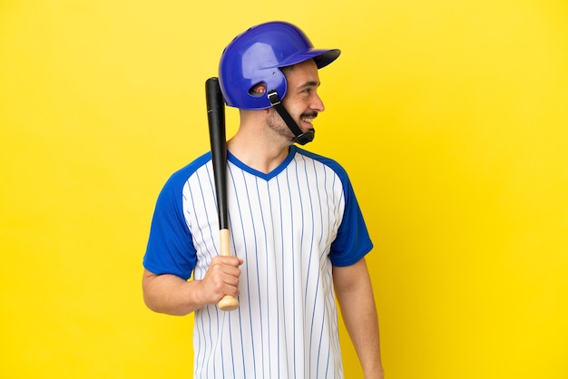 Jonge blanke man die honkbal speelt geïsoleerd op gele achtergrond lachend in zijpositie