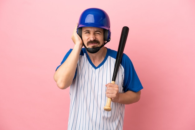 Jonge blanke man die honkbal speelt geïsoleerd op roze achtergrond gefrustreerd en die oren bedekt