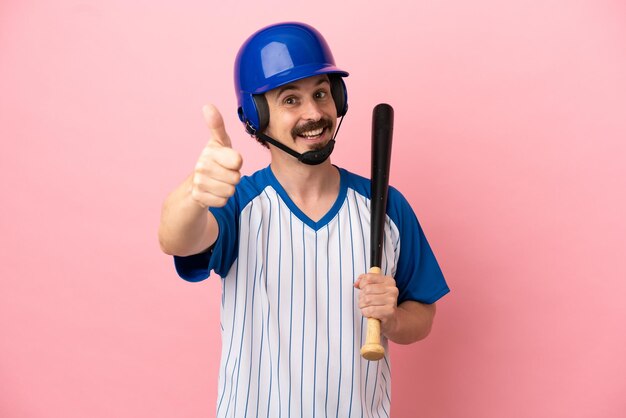 Jonge blanke man die honkbal speelt geïsoleerd op roze achtergrond met duimen omhoog omdat er iets goeds is gebeurd