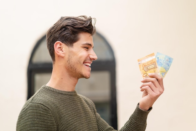 Jonge blanke man die veel geld meeneemt naar buiten met een gelukkige uitdrukking