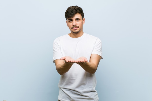 Jonge blanke man draagt een witte t-shirt bedrijf iets met palmen, aanbieden aan camera.