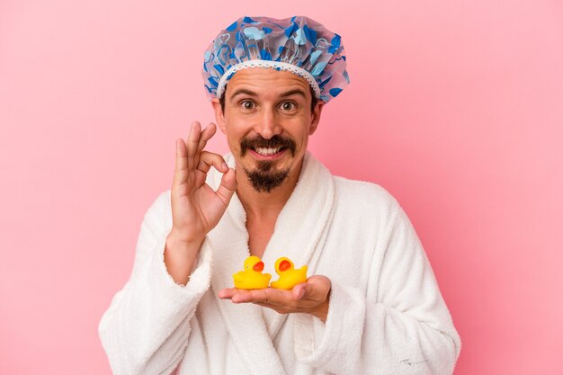 Jonge blanke man gaat naar de douche met rubberen eenden geïsoleerd op een roze achtergrond, vrolijk en zelfverzekerd met een goed gebaar.