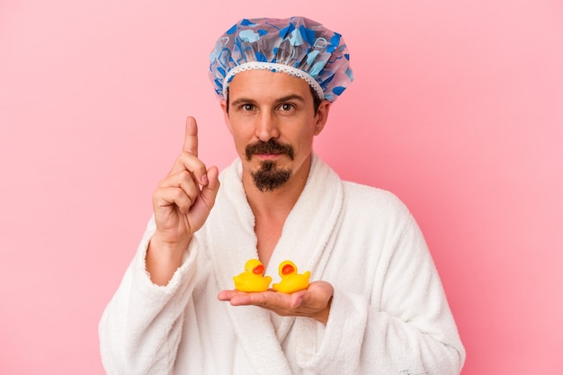 Jonge blanke man gaat naar de douche met rubberen eenden geïsoleerd op roze achtergrond met nummer één met vinger.