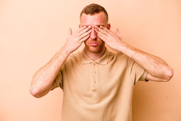 Jonge blanke man geïsoleerd op beige achtergrond bang die ogen bedekt met handen