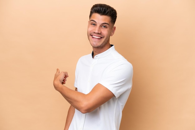 Jonge blanke man geïsoleerd op beige achtergrond die terug wijst