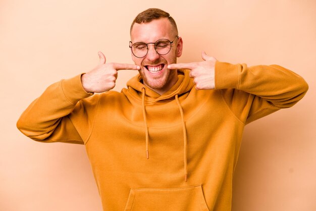 Foto jonge blanke man geïsoleerd op beige achtergrond glimlacht wijzende vingers naar mond