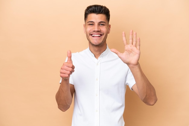 Jonge blanke man geïsoleerd op beige achtergrond telt zes met vingers