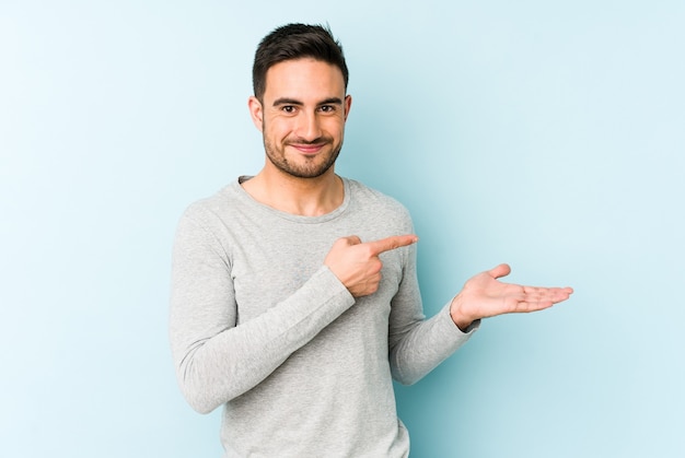 Jonge blanke man geïsoleerd op blauw opgewonden met een kopie ruimte op palm.