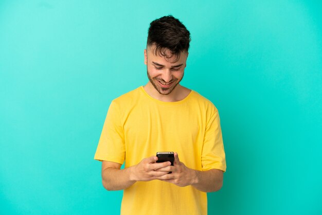Jonge blanke man geïsoleerd op blauwe achtergrond die een bericht verzendt met de mobiel