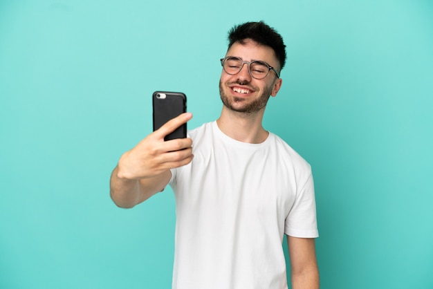 Jonge blanke man geïsoleerd op blauwe achtergrond die een selfie maakt met mobiele telefoon