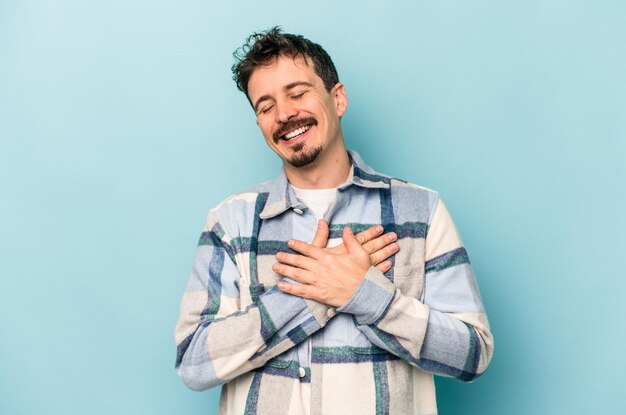 Jonge blanke man geïsoleerd op blauwe achtergrond lachen houden handen op hart concept van geluk