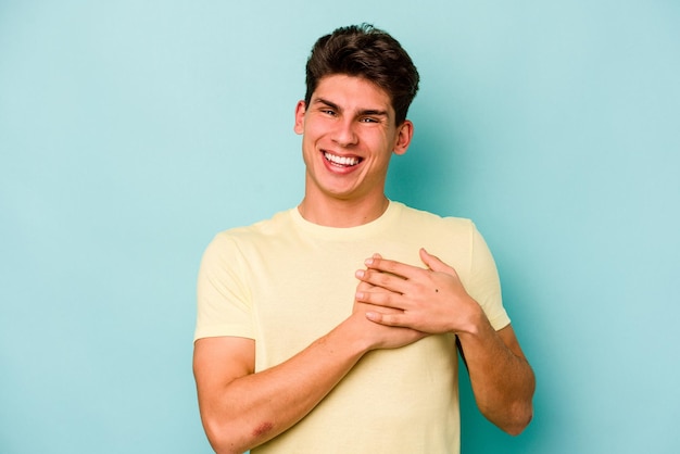 Jonge blanke man geïsoleerd op blauwe achtergrond lachen houden handen op hart concept van geluk