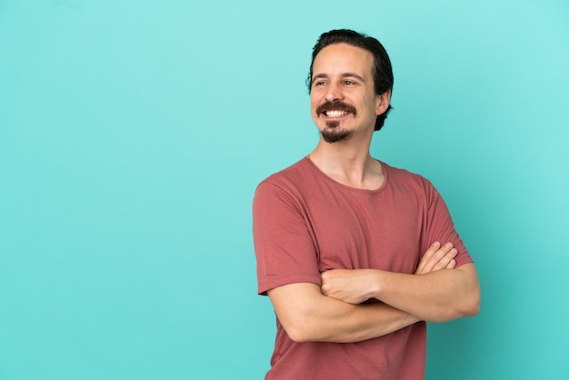 Jonge blanke man geïsoleerd op blauwe achtergrond met gekruiste armen en happy