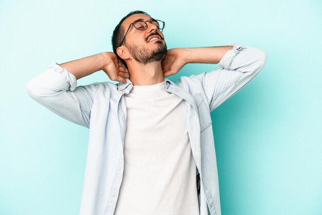 Jonge blanke man geïsoleerd op blauwe achtergrond voelt zich zelfverzekerd met handen achter het hoofd