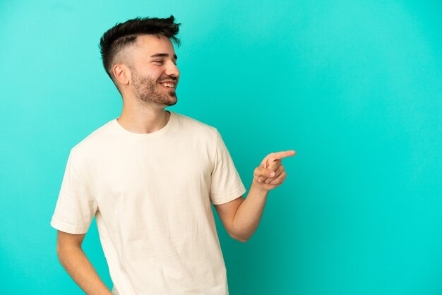 Jonge blanke man geïsoleerd op een blauwe achtergrond die met de vinger naar de zijkant wijst en een product presenteert