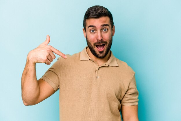 Foto jonge blanke man geïsoleerd op een blauwe achtergrond persoon die met de hand wijst naar een shirt kopieerruimte trots en zelfverzekerd?