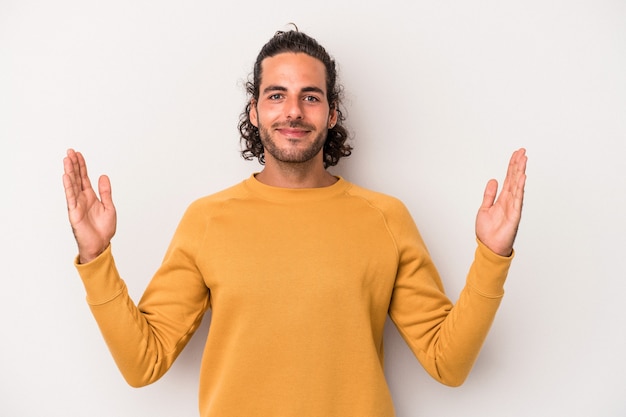 Jonge blanke man geïsoleerd op een grijze achtergrond met iets kleins met wijsvingers, glimlachend en zelfverzekerd.