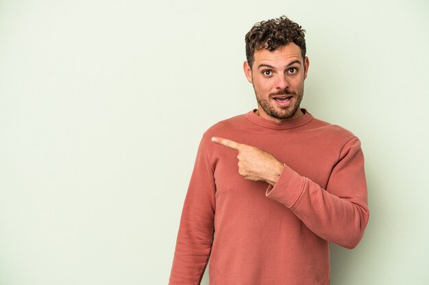 Foto jonge blanke man geïsoleerd op een groene achtergrond die naar de zijkant wijst