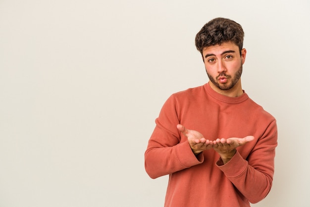 Jonge blanke man geïsoleerd op een witte achtergrond die lippen vouwt en handpalmen vasthoudt om luchtkus te sturen.