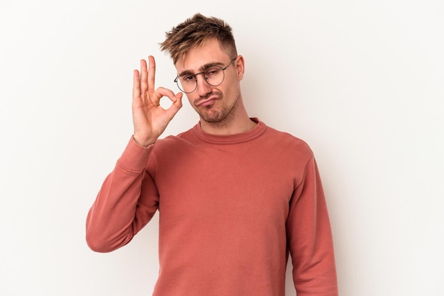 Jonge blanke man geïsoleerd op een witte achtergrond knipoogt en houdt een goed gebaar met de hand.