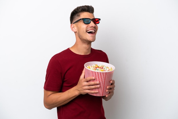 Jonge blanke man geïsoleerd op een witte achtergrond met 3D-bril en met een grote emmer popcorns