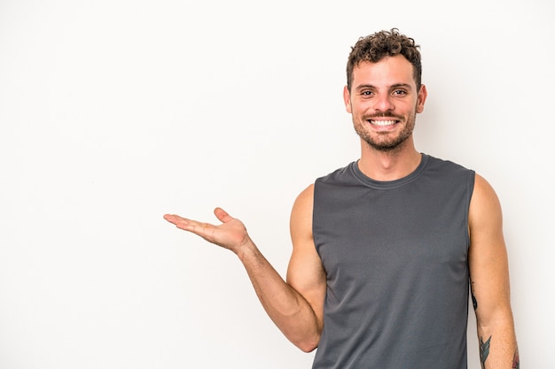 Jonge blanke man geïsoleerd op een witte achtergrond met een kopie ruimte op een palm en met een andere hand op de taille.