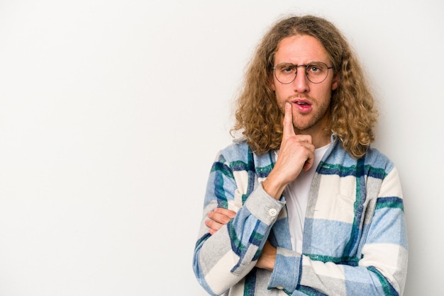 Jonge blanke man geïsoleerd op een witte achtergrond zijwaarts kijkend met twijfelachtige en sceptische uitdrukking