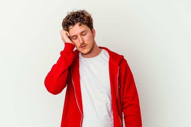 Jonge blanke man geïsoleerd op een witte muur moe en erg slaperig hand op het hoofd houden.