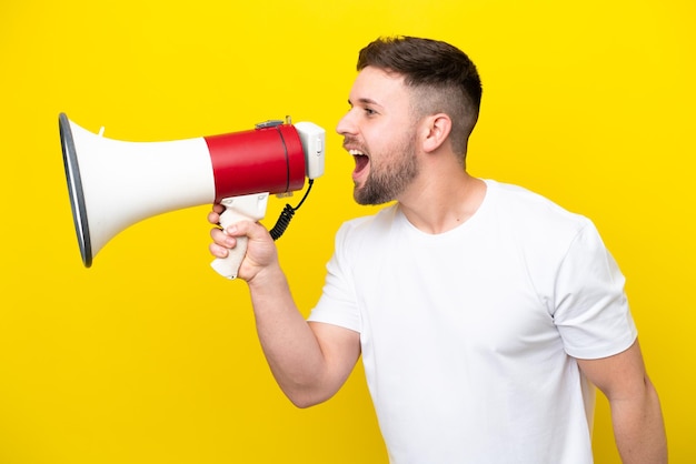 Jonge blanke man geïsoleerd op gele achtergrond die door een megafoon schreeuwt om iets in zijpositie aan te kondigen
