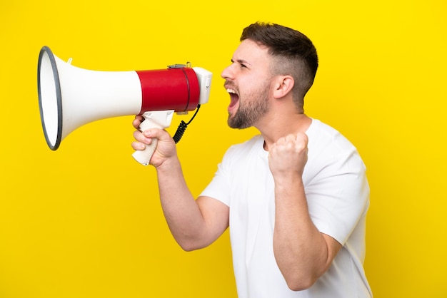 Jonge blanke man geïsoleerd op gele achtergrond die door een megafoon schreeuwt om iets in zijpositie aan te kondigen