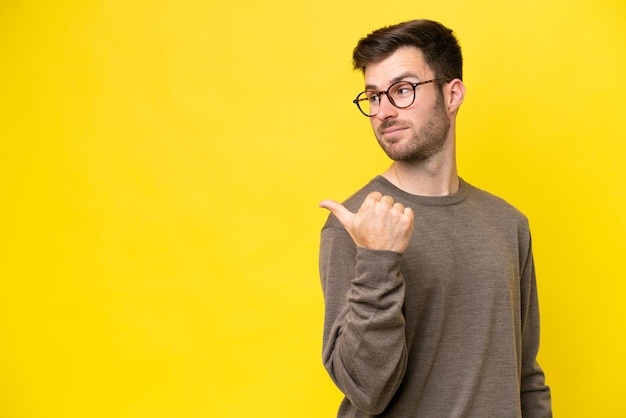 Jonge blanke man geïsoleerd op gele achtergrond die naar de zijkant wijst om een product te presenteren