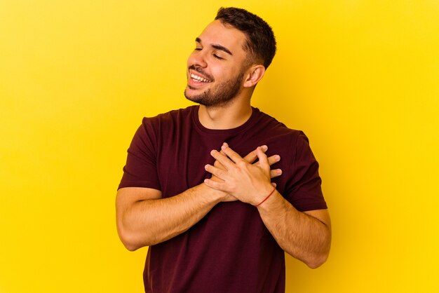 Jonge blanke man geïsoleerd op gele achtergrond heeft een vriendelijke uitdrukking, handpalm tegen de borst te drukken. Liefde concept.