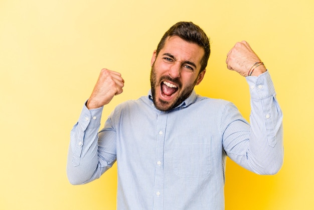 Jonge blanke man geïsoleerd op gele achtergrond juichen zorgeloos en opgewonden Victory concept