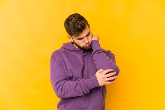 Jonge blanke man geïsoleerd op gele achtergrond masserende elleboog, lijden na een slechte beweging.