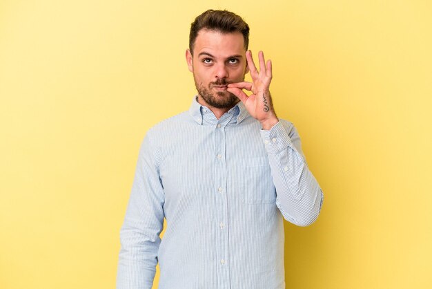 Jonge blanke man geïsoleerd op gele achtergrond met vingers op lippen die een geheim houden.