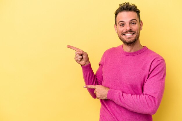 Jonge blanke man geïsoleerd op gele achtergrond opgewonden wijzend met wijsvingers weg.